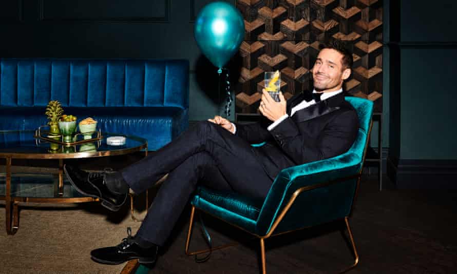 Spencer Matthews, smiling, reclining in a chair with a drink in one hand and a balloon in the other