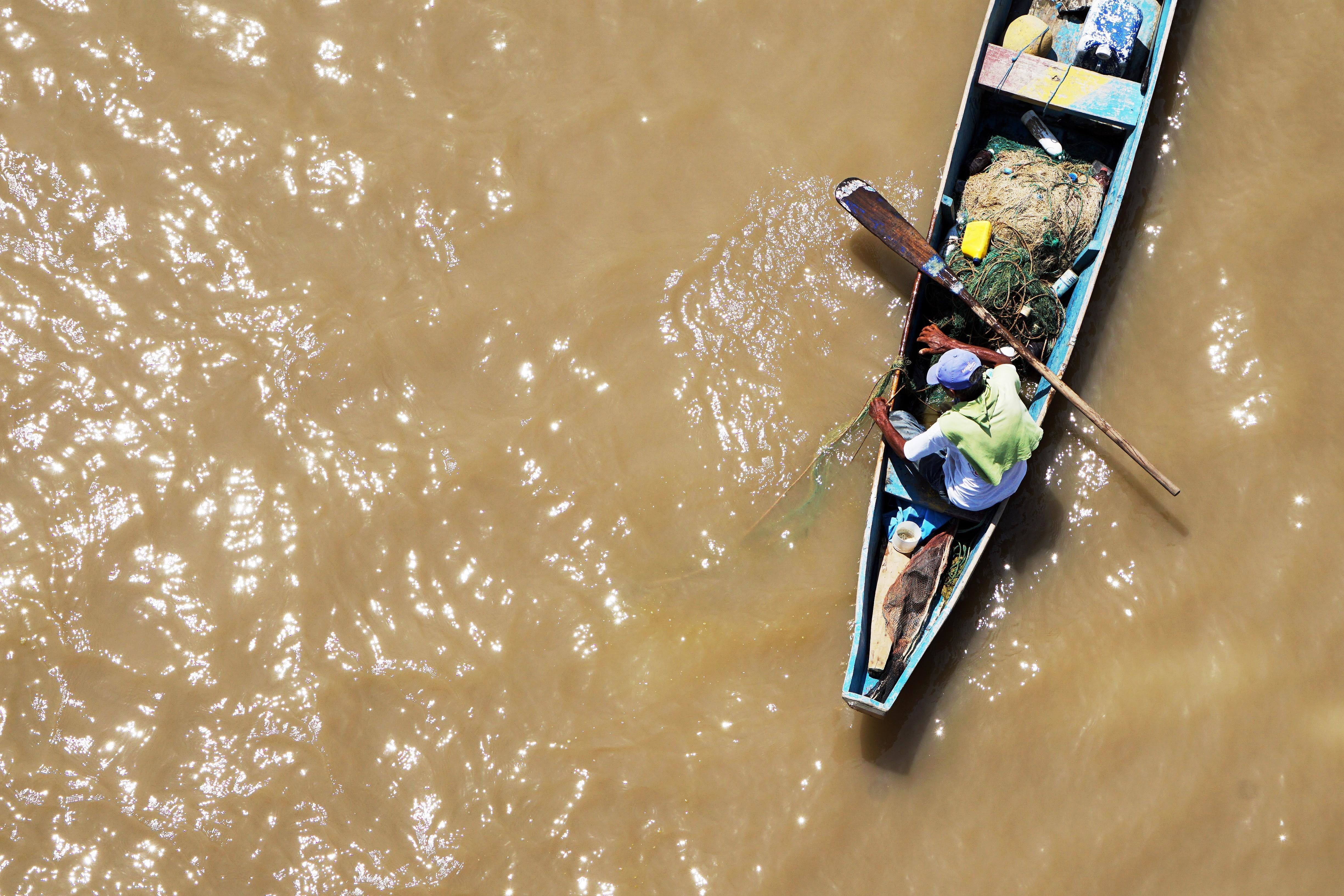 a fishman paddles his boat in a muddy river 