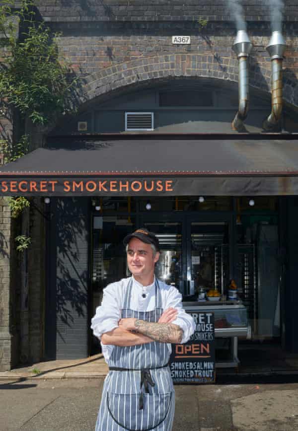 Max Bergius in a striped apron standing outside Secret Smokehouse, built in a railway arch with two steel chimneys and a large awning