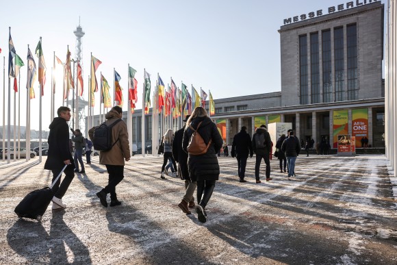 Trade visitors on their way to FRUIT LOGISTICA. The photo shows the north entrance to the Berlin exhibition grounds. Waving flags and the Funkturm can be seen in the background