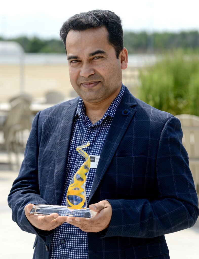 Man in a blue suit holds a glass award with a flat base and a spiral of glass with a yellow ribbon within the glass spiral.