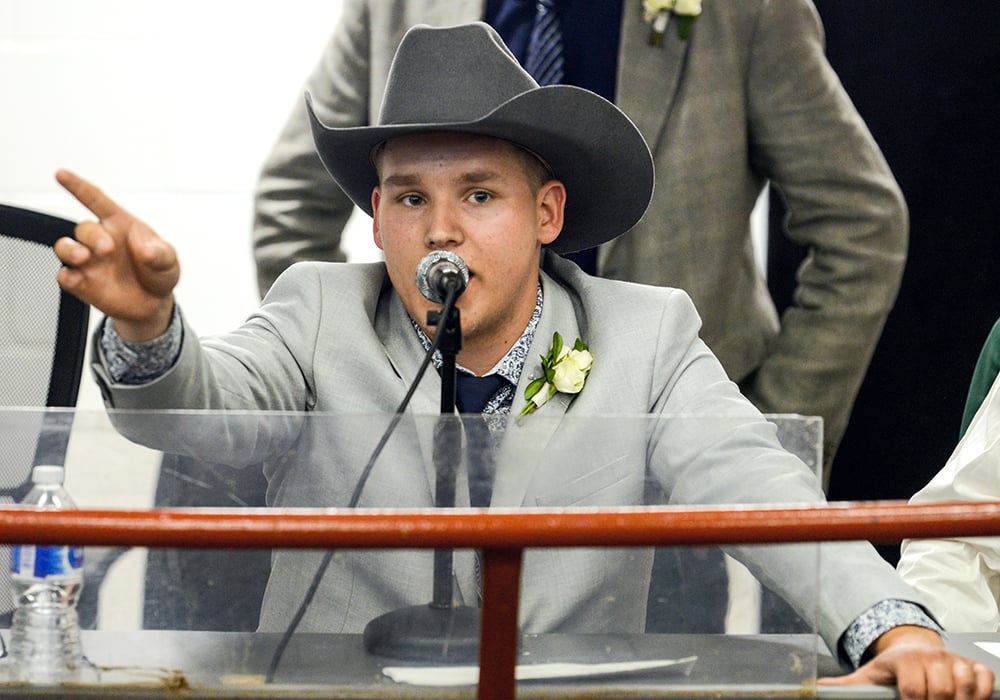 A man in a light suit jacket and charcoal coloured cowboy hat chants into the microphone while pointing out bids