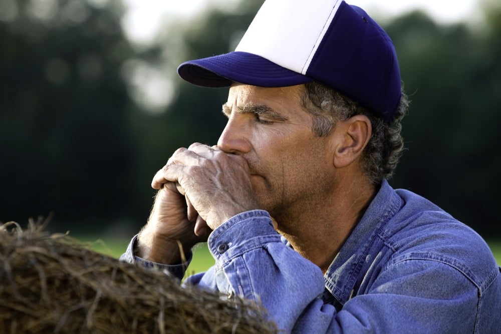 Worried farmer leaning on bale