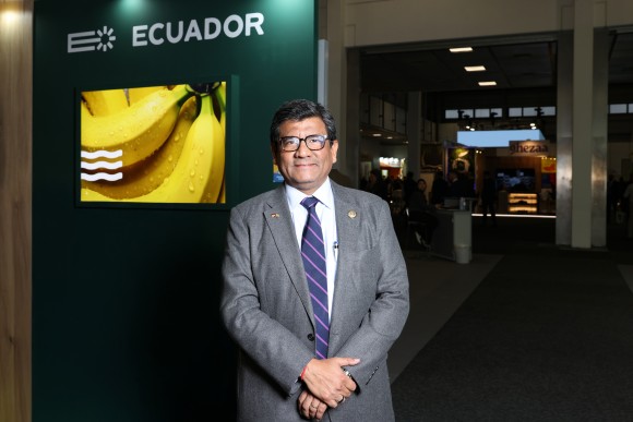 A man stands at a trade fair stand and looks friendly into the camera.