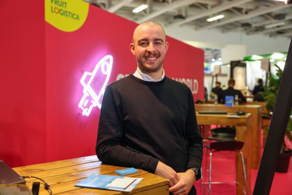 A man stands in front of a red background with a glowing rocket and smiles.