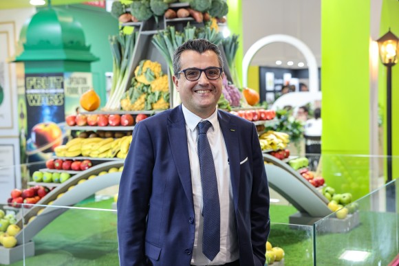 A man in a blue suit stands in front of a large structure filled with fruit and vegetables. 