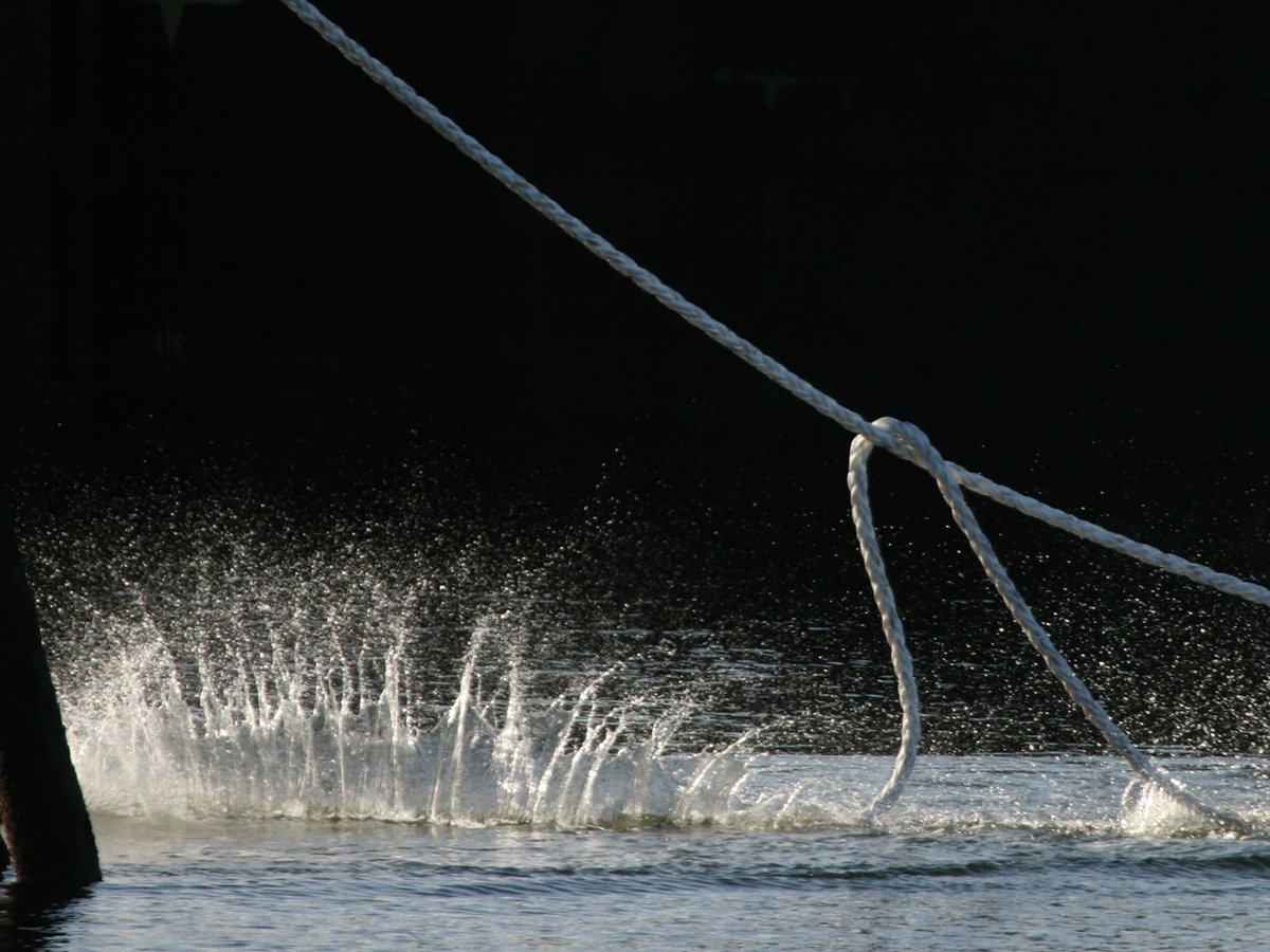 Close-up of water splashing as a mooring line is pulled taught by unseen crew on a large ship at port.