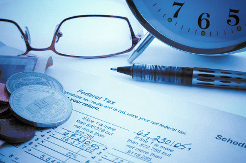 Close-up of glasses, change, a pen and an alarm clock on top of some tax forms on a table.