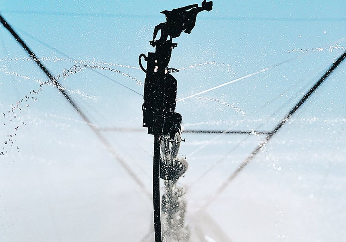 Close-up of a sprinkler head on an irrigation pivot with water flowing out of it.