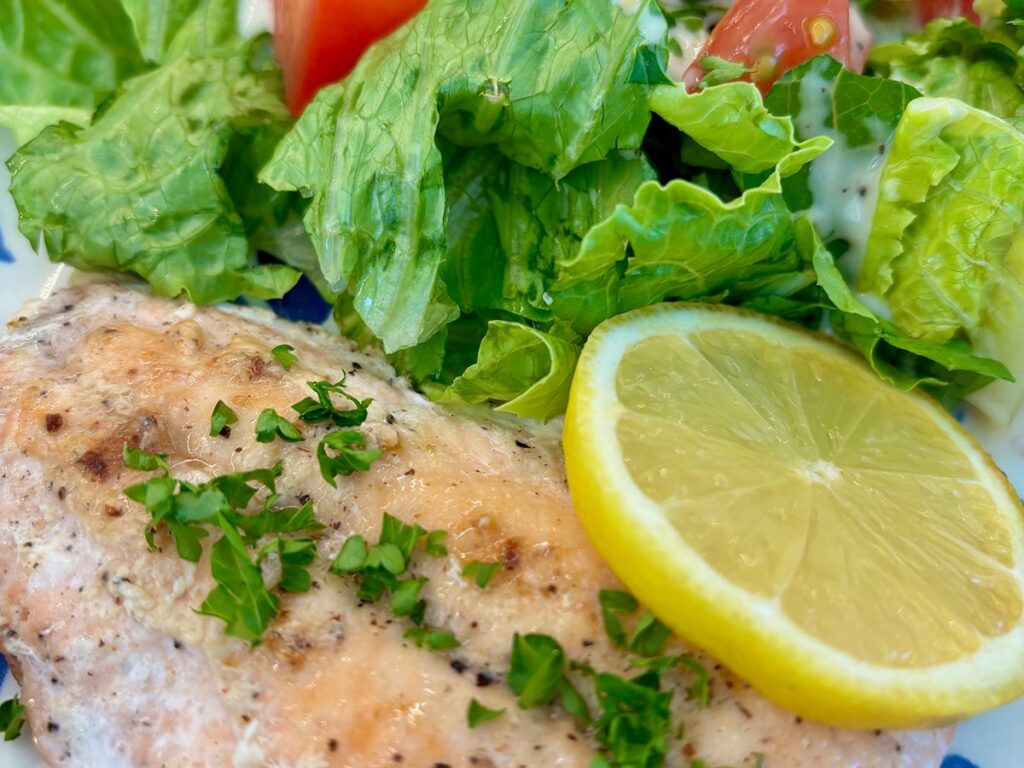 Oven roasted salmon teamed with herbs and lemon and a side of greens on a plate.