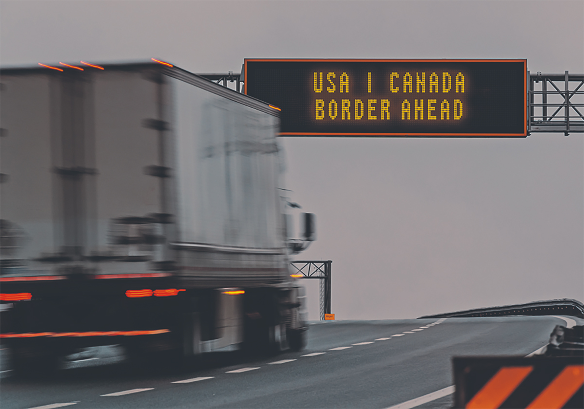 A semi truck moves down a highway about to pass beneath a sign that reads, 
