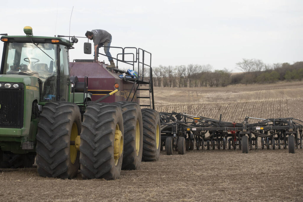 A farmer is working on top of his air seeder in the middle of a field.