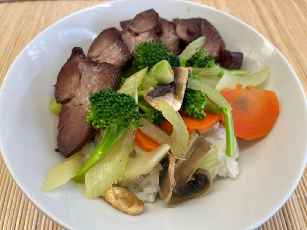 Barbecued pork served with stir-fried vegetables on a bed of rice.