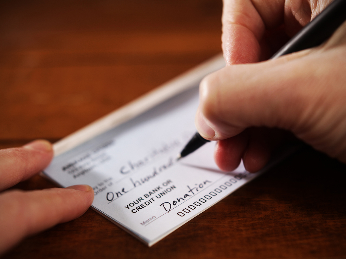 Close-up of a hand holding a pen writing the dollar amount on a cheque.