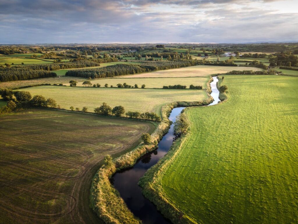 An aerial photo of a small stream running though agricultural land in the summertime.