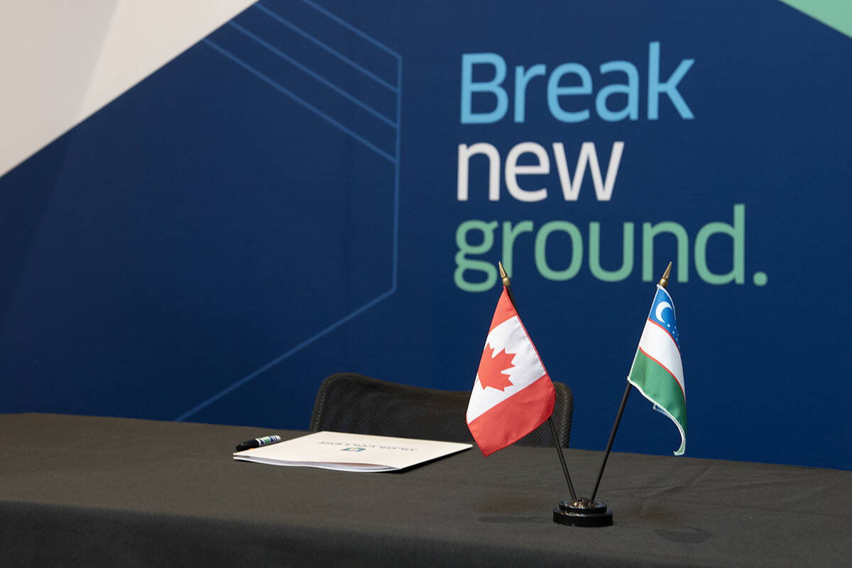 Small flags of both Canada and Uzbekistan sit on a desk with a backdrop that reads 