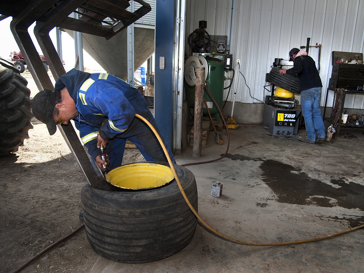 Two farm workers work on implement tires in a shop during seeding.