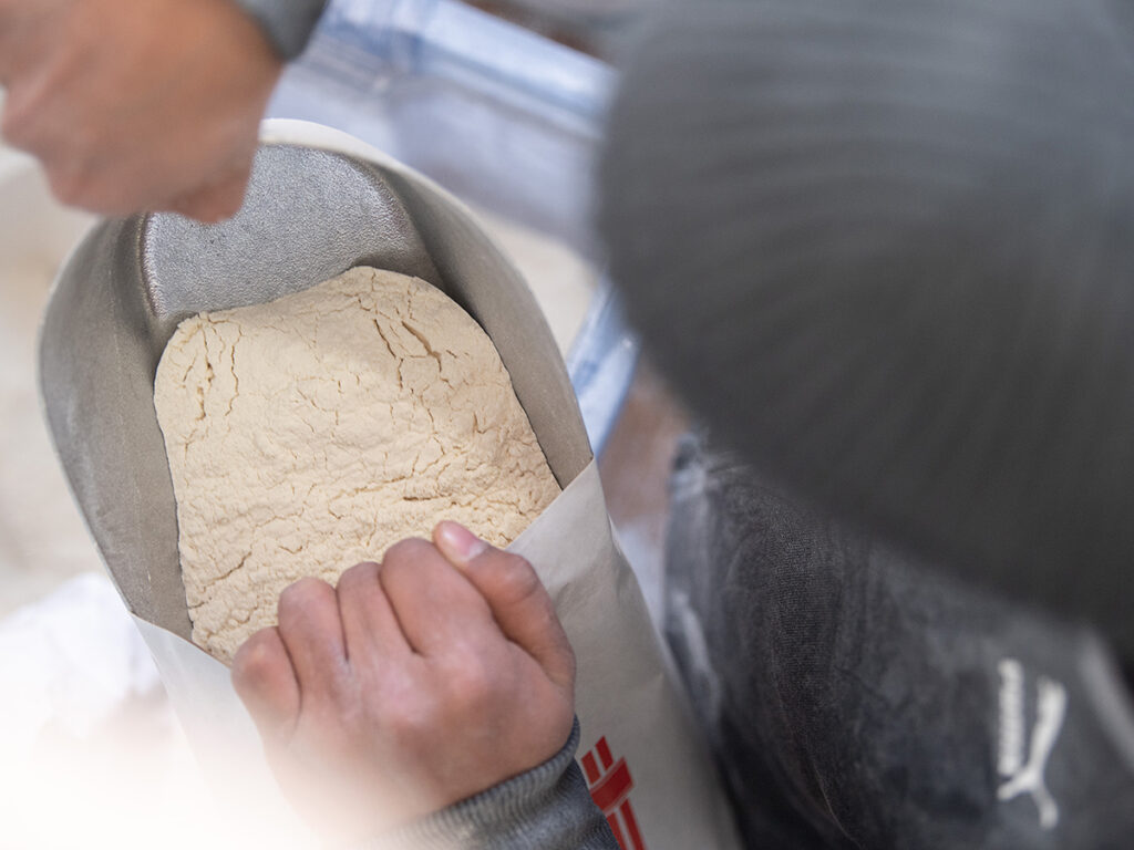 Overhead view of someone looking into a bag of flour, holding the bag open with their hands.