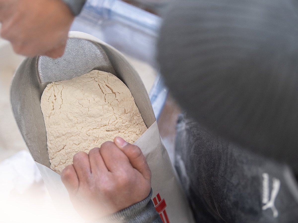 Overhead view of someone looking into a bag of flour, holding the bag open with their hands.