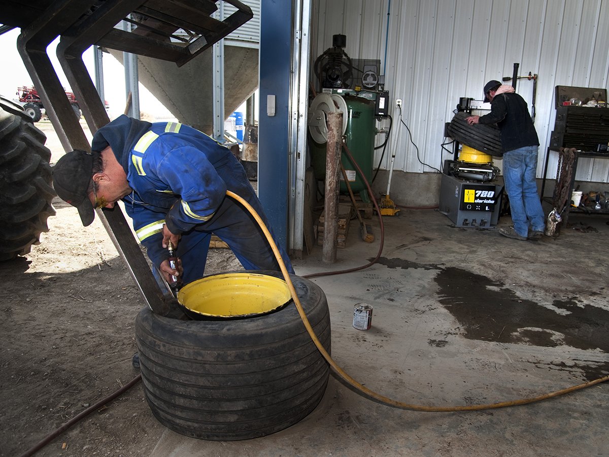 Two farm workers work on implement tires in a shop during seeding.