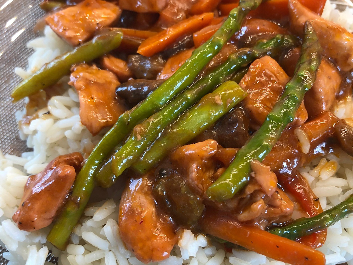 Pieces of asparagus in a stir fry on a bed of rice on a plate.