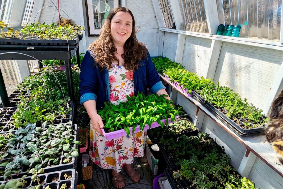 Kristen Raney poses, holding a tray of plants, in her small greenhouse.