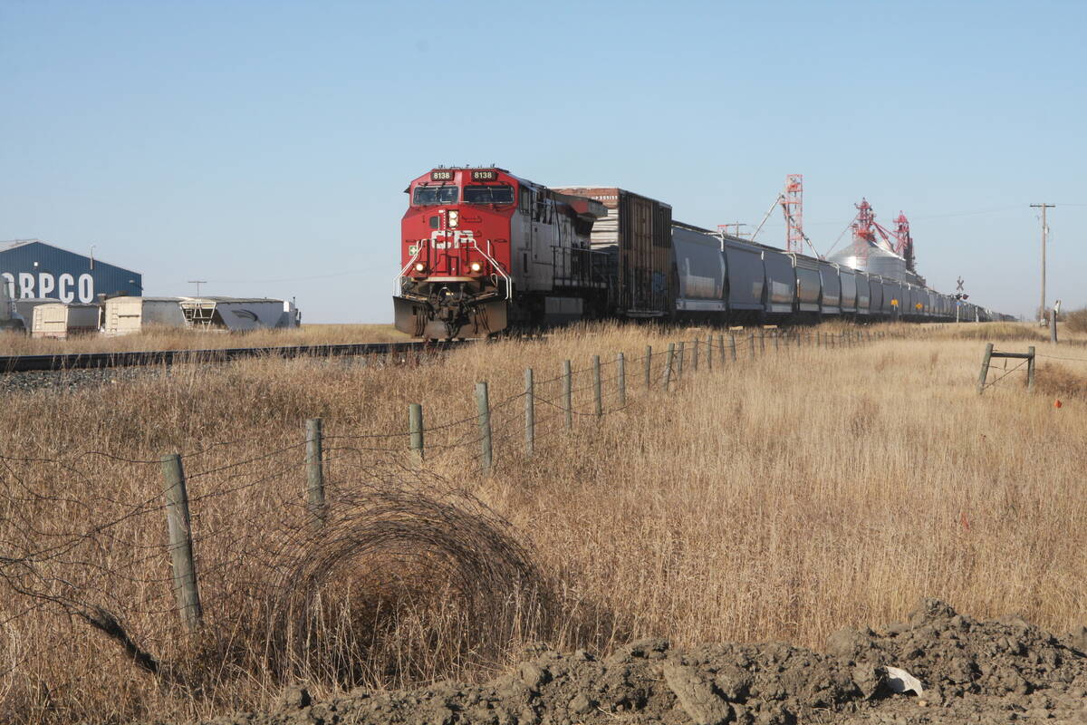 A CP locomotive pulls grain cars past an inland grain terminal.