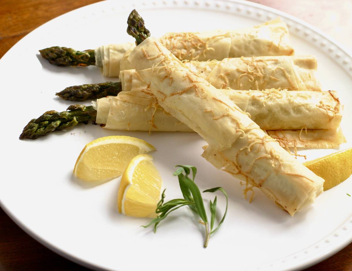 Asparagus spears wrapped in phyllo pastry laying on a plate with two lemon wedges.