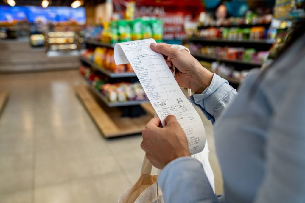 Looking over the shoulder of a female shopper in a grocery story as she examines her till receipt.