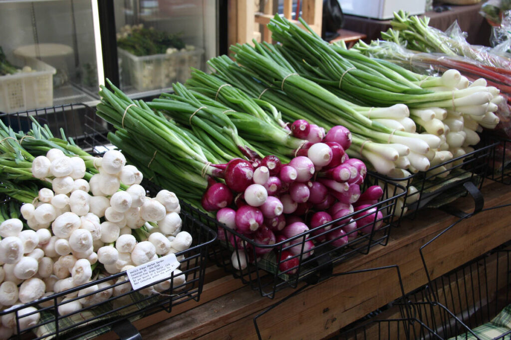 Several varieties of onions and some garlic on display in baskets at a market.