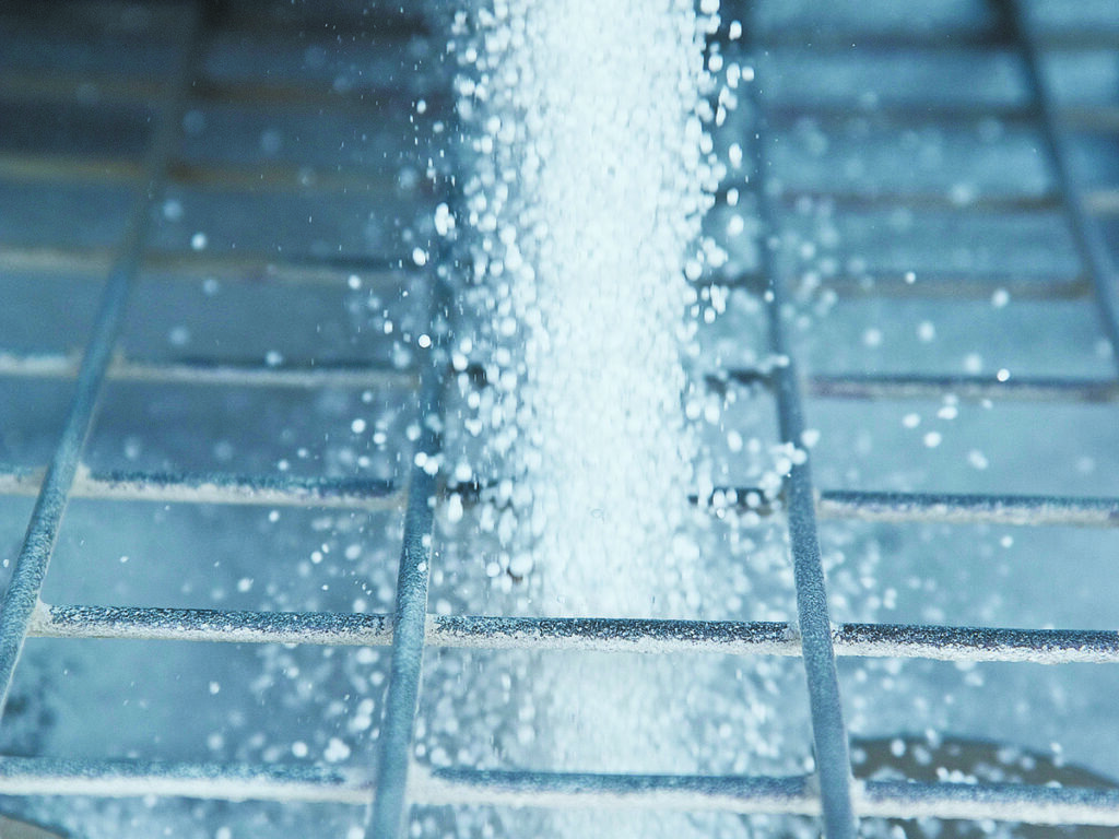 Close-up of the white granules of fertilizer pouring through the grate on an auger