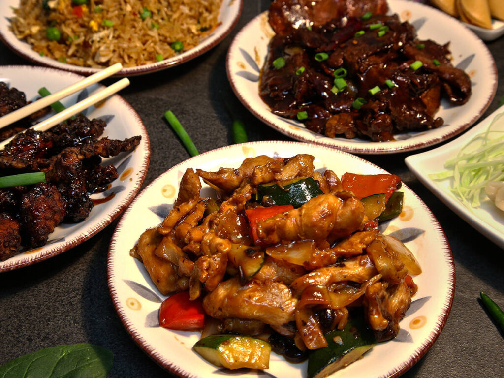 A stock photo of various plates on a table, each holding a different Asian-style food.