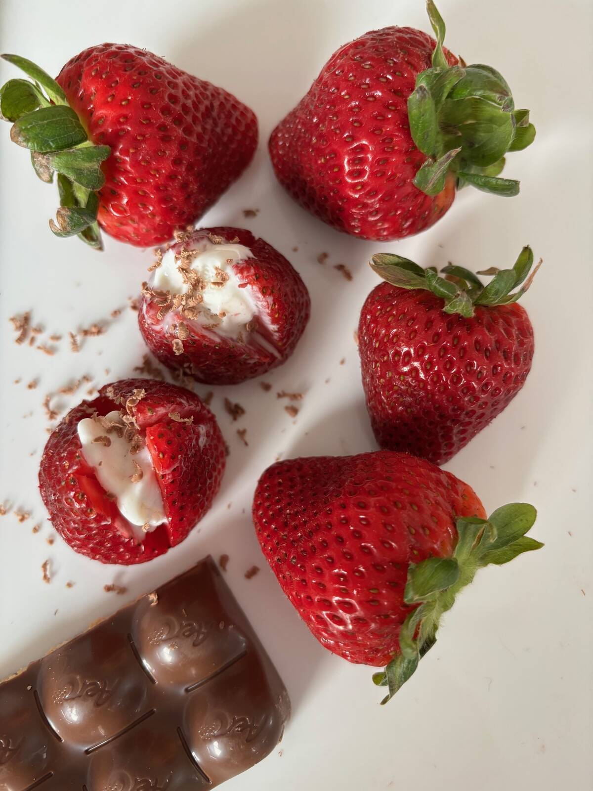 Bright red strawberries stuffed with cream sit on a white surface.