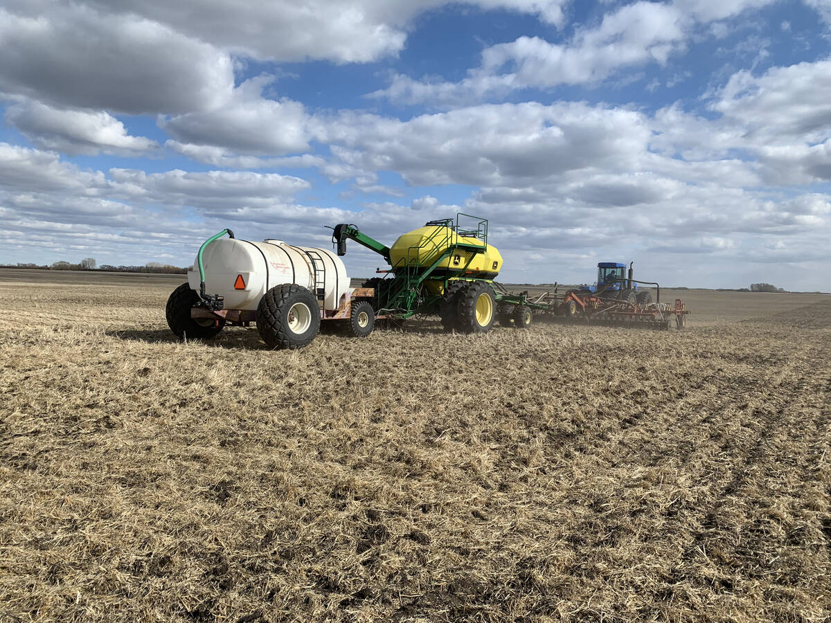 An air seeder rig seeds red lentils on a sunny day, with a number of pillowy white clouds in the sky, southeast of Delisle, Saskatchewan.
