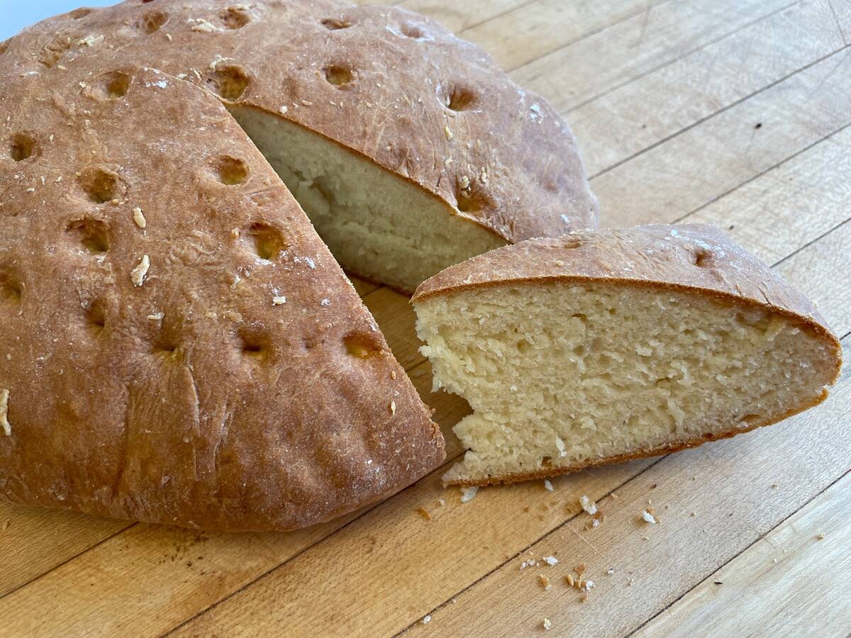 A fresh bannock loaf sitting on a counter with a triangular wedge cut out of it and set by its side.