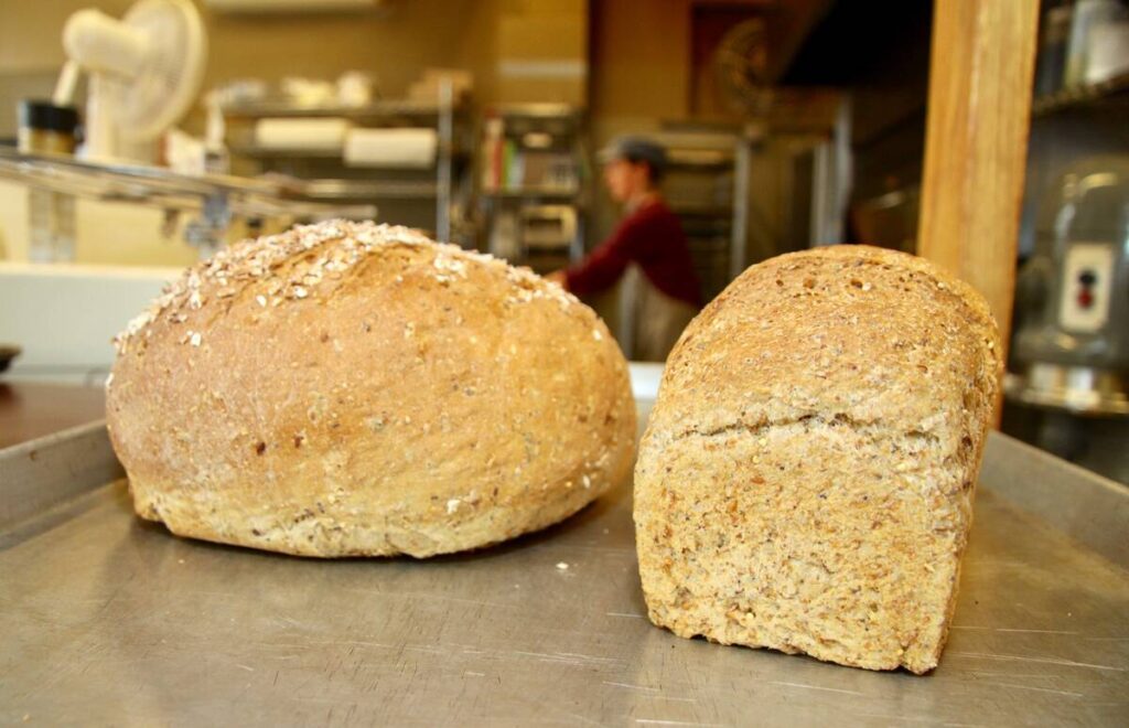 Two freshly-baked loaves of bread sit on a stainless steel counter in a bakery.
