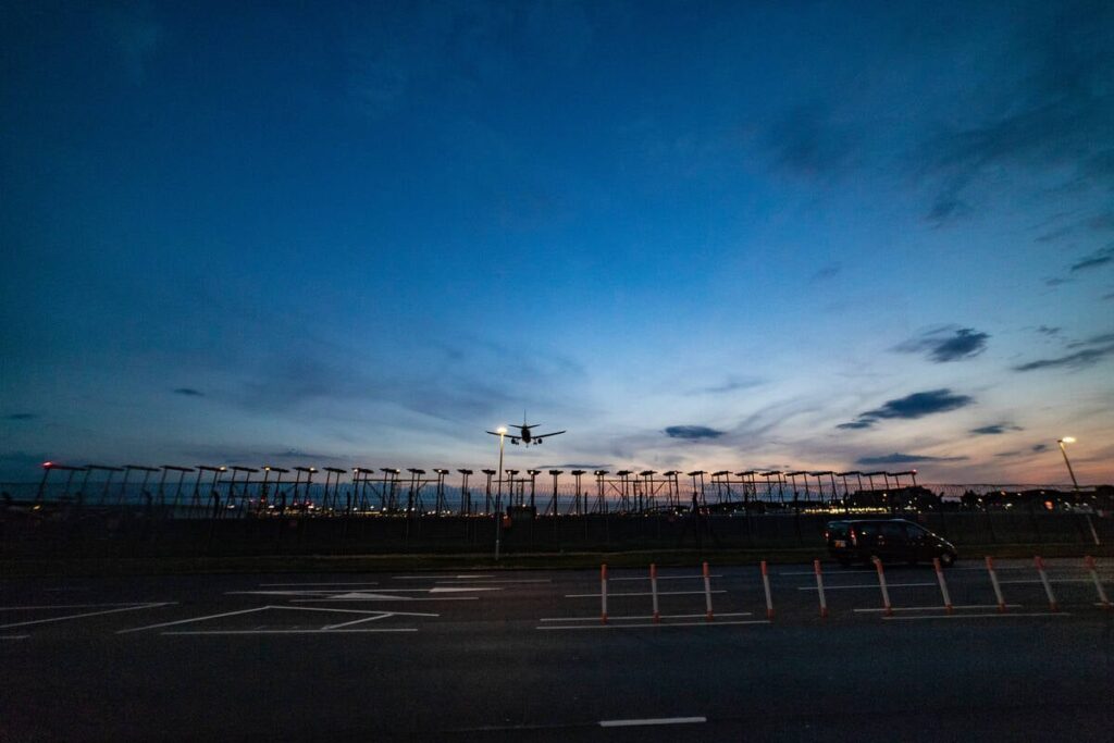 Photo taken from the end of a runway just after sunset as a large passenger jet passes overhead as it is about to land.