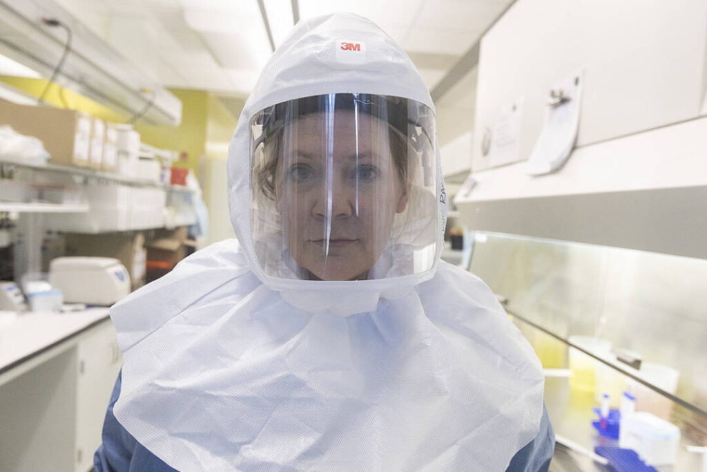 Close-up of a researcher wearing a sealed helmet and face shield at work in a lab that handles infectious diseases.