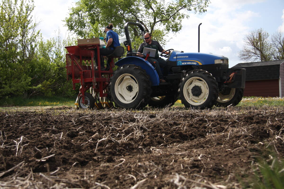 A man drives a small blue tractor while a woman sits atop a crop plot seeder at the Ag in Motion farm show site near Langham, Sask.