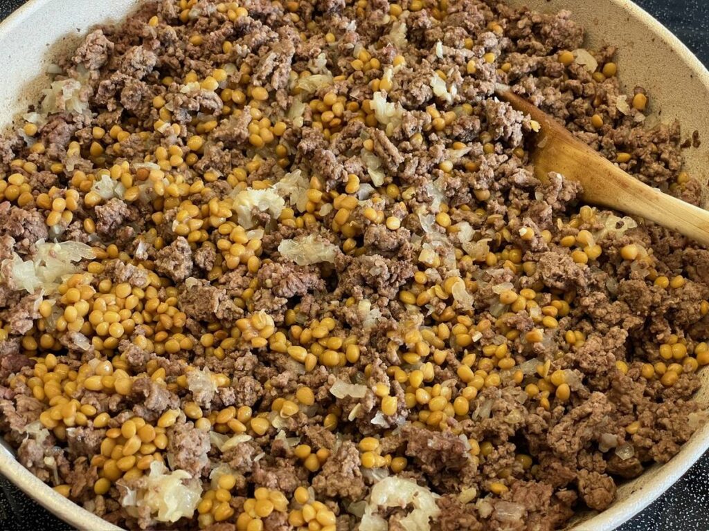 A big batch of ground beef, with cooked lentils mixed in, in a skillet.