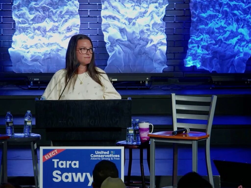United Conservative Party candidate Tara Sawyer speaks to a room of people from a lecturn on the campaign trail prior to the byelection she would go on to win on June 23, 2025.