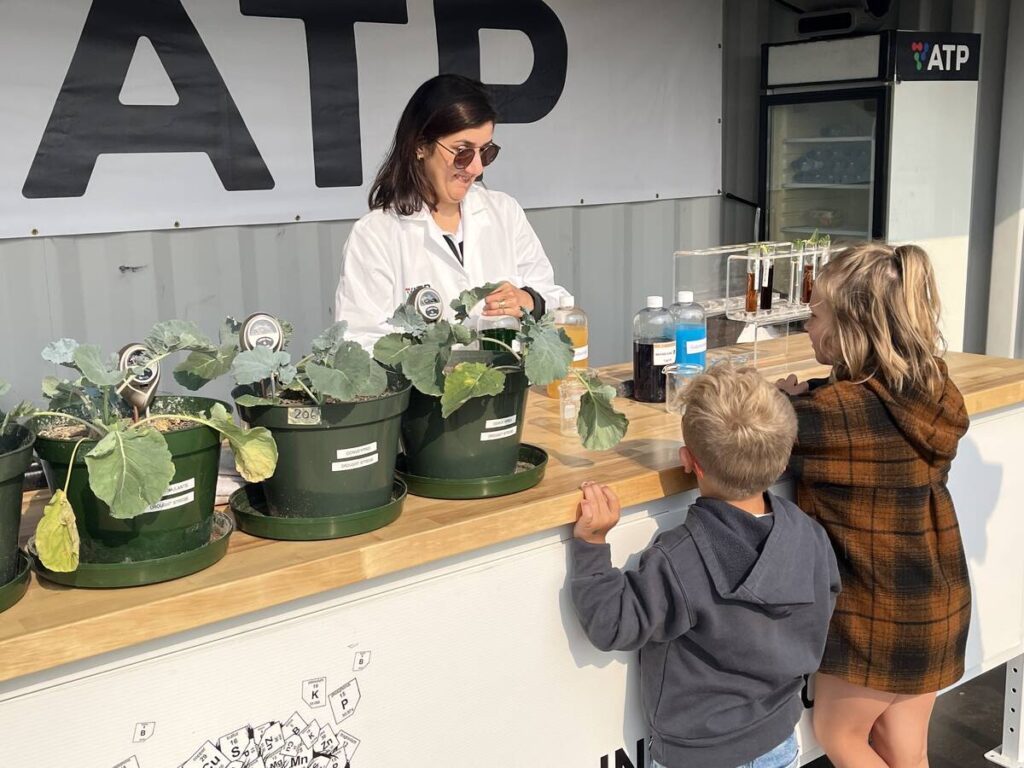 Barbara Hodecker, director of research and development for ATP Nutrition shows youth Blair and Eleanor Uruski how biostimulants help plants handle abiotic stress like drought.