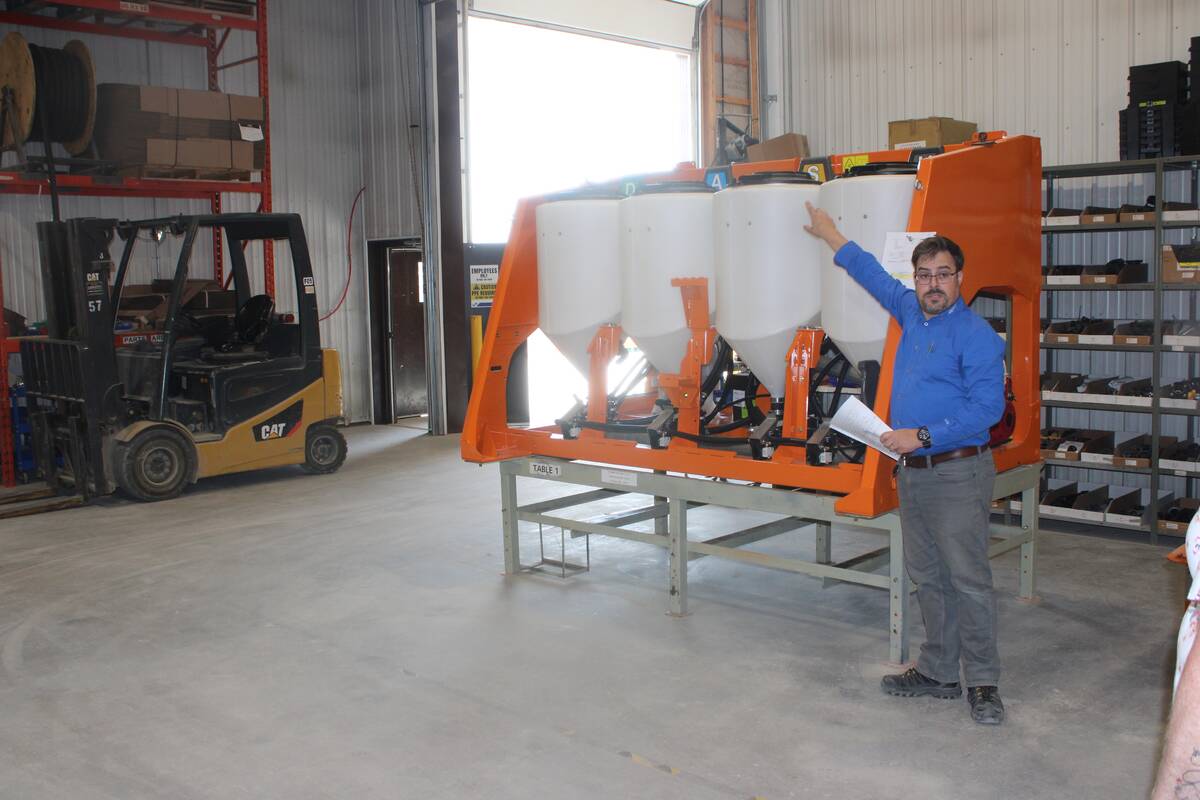 A PhiBer employee points toward four white, plastic product storage tanks mounted in an orange metal frame.