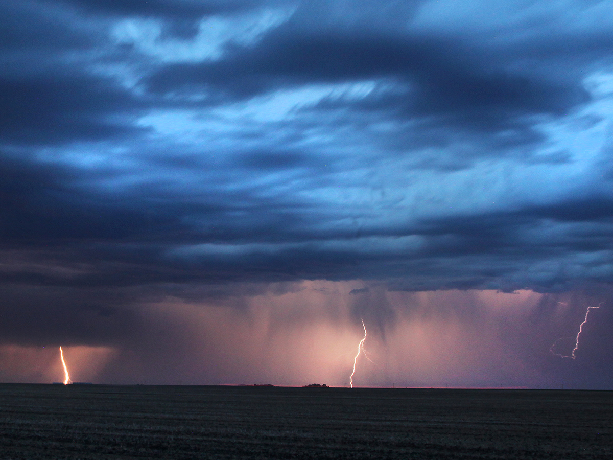 Several strokes of lightning arc downward from an angry dark cloud in the distance near dusk.
