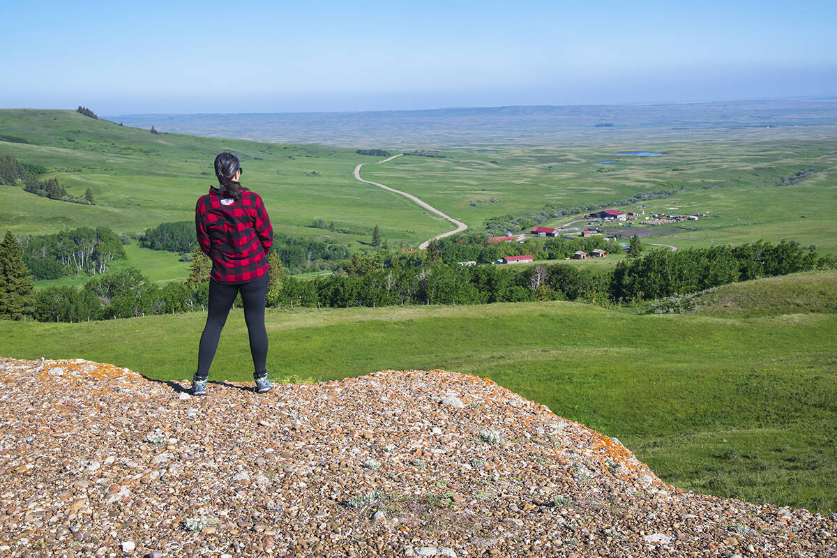 A woman stands near the edge of a valley, looking over the Reesor Ranch from a hike into the hills.