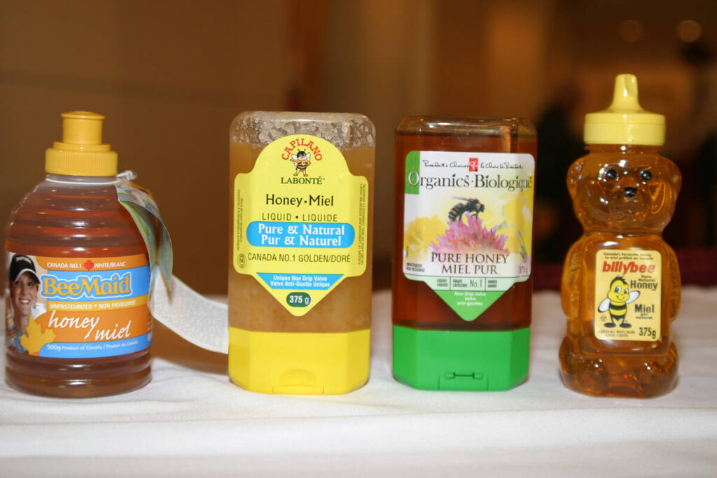 Four containers of honey - only one of which is actually a product of Canada - sit on a white tablecloth.