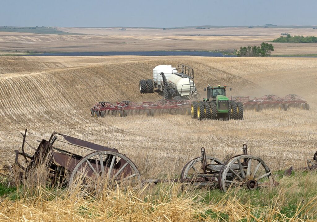 A seeder and tractor pass over rolling hills in the Prairie pothole region.