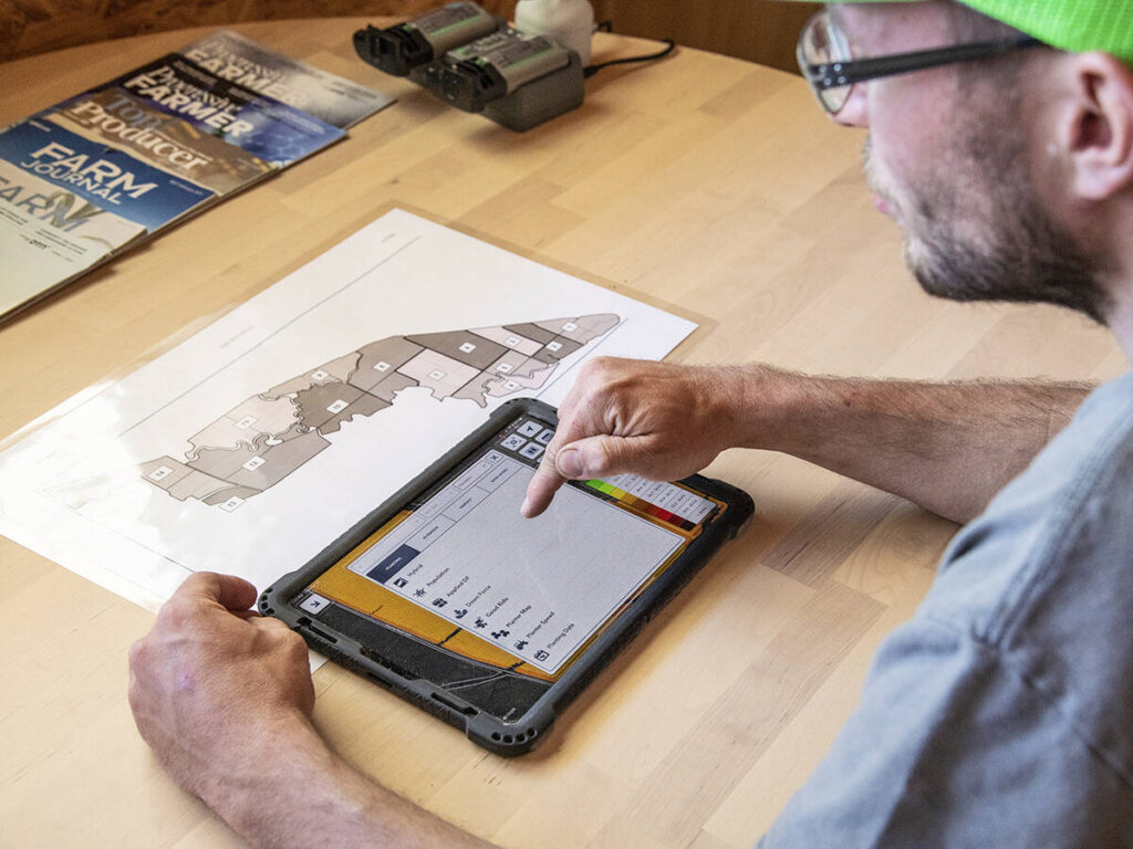 A farmer is seen using a smart device to review data and plan his customized seed application for the day.