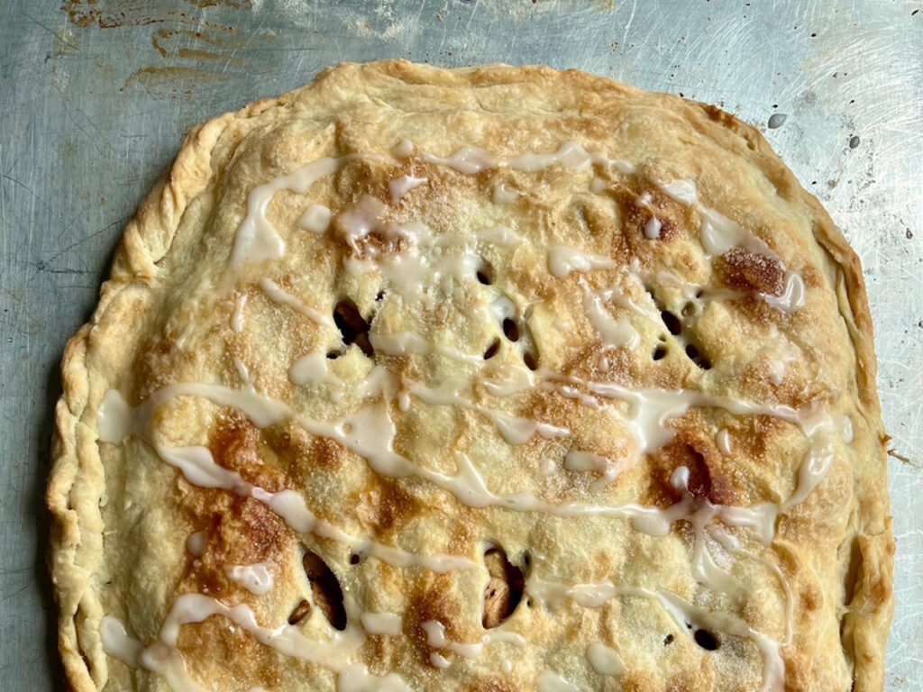 An apple pastry seen from above, fresh out of the oven and still on a metal baking sheet.