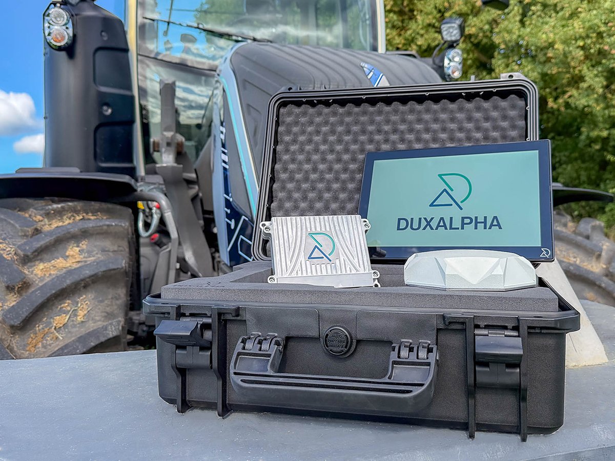 A hardened dark gray case with a tablet in it with a "Duxalpha" logo on its screen sits on a flat surface in front of a large tractor.